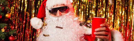Santa claus in sunglasses holding plastic cup under confetti near tinsel, bannerの写真素材