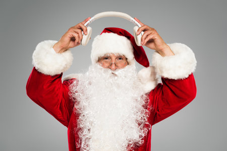 Father christmas in costume holding wireless headphones isolated on greyの写真素材