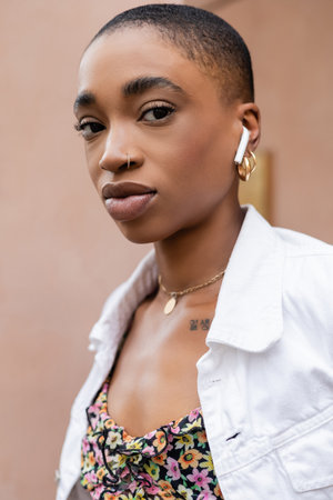 Trendy african american woman in earphone looking at camera outdoorsの写真素材