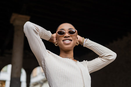 Low angle view of smiling short haired african american woman in sunglasses standing outdoors