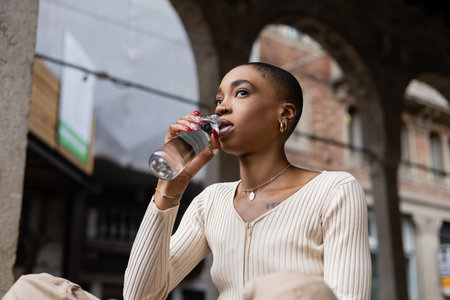 Short haired african american woman holding bottle of water on urban street in Treviso
