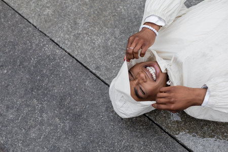 Top view of cheerful african american woman in raincoat lying on urban streetの写真素材