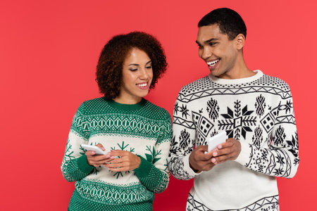 cheerful african american man showing mobile phone to smiling girlfriend isolated on red