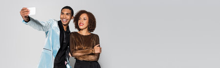 happy african american man in elegant blazer taking selfie with young girlfriend isolated on grey,...