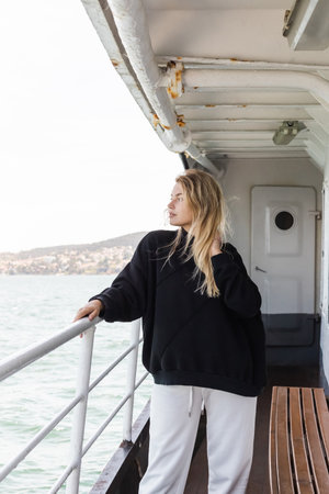 blonde woman in black sweater looking at sea from ferry boat crossing bosporus in istanbul