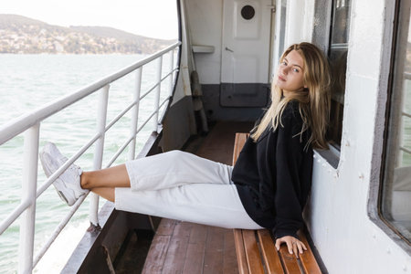 blonde woman in black sweater sitting on bench in ferry boat crossing bosporus in istanbul