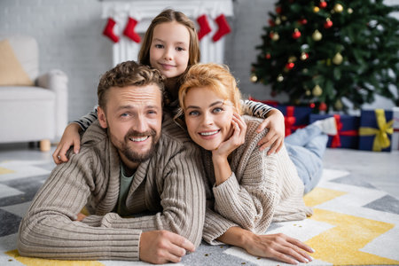 Cheerful girl hugging parents near confetti on floor during christmasの写真素材