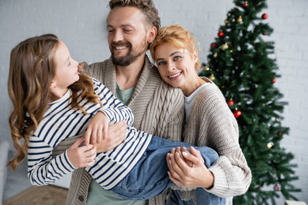 Smiling parents in warm cardigans holding daughter during new year celebration at homeの写真素材