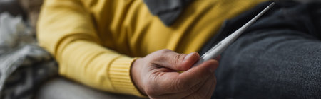 partial view of diseased man holding electronic thermometer while lying on blurred background,...