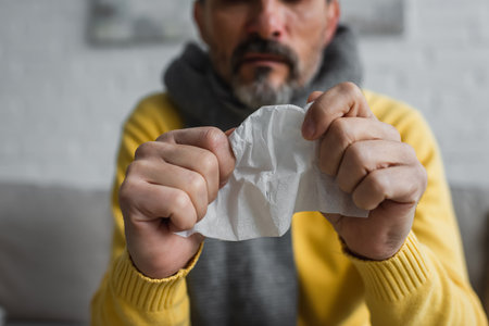selective focus of crumpled paper napkin in hands of cropped diseased man on blurred backgroundの写真素材