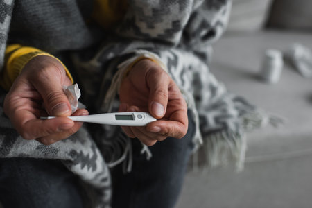 partial view of diseased man holding electronic while suffering from fever