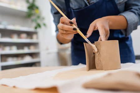 cropped view of african american woman in apron holding shaper while modeling clay