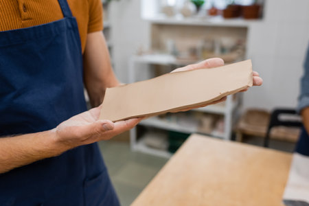 cropped view of man in apron holding rectangle shape clay piece in handsの写真素材