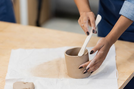 partial view african american woman with manicure modeling clay cup with shaper during pottery classの写真素材