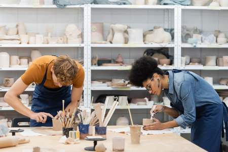 multiethnic woman and man shaping clay cups during pottery classの写真素材