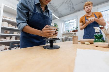 african american woman molding clay cup near blurred and redhead man
