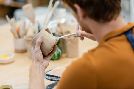 Young craftsman painting on clay cup in pottery workshopの写真素材