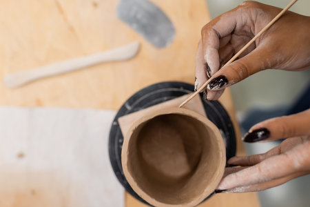 Top view of african american craftswoman making ceramic product with wooden stick in pottery studioの写真素材