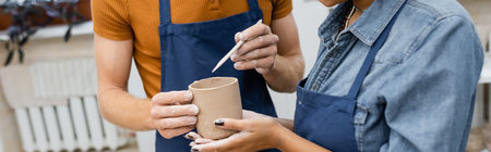 cropped view of african american woman near man in apron modeling clay cup with shaper, banner