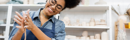 Positive african american craftswoman in apron forming clay in workshop, bannerの写真素材