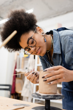 Smiling african american craftswoman making clay sculpture in pottery studioの写真素材