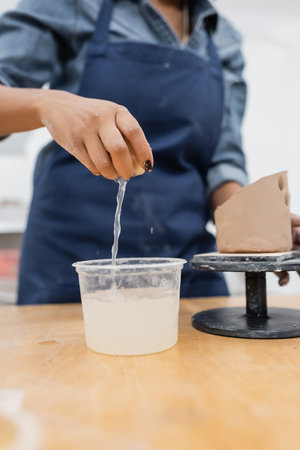 Cropped view of african american craftswoman holding sponge with water near clay in pottery studioの写真素材