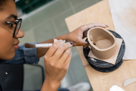 High angle view of african american sculptor making holes in clay product in workshopの写真素材