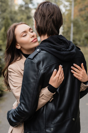 young and pretty woman in coat hugging boyfriend in black jacketの写真素材