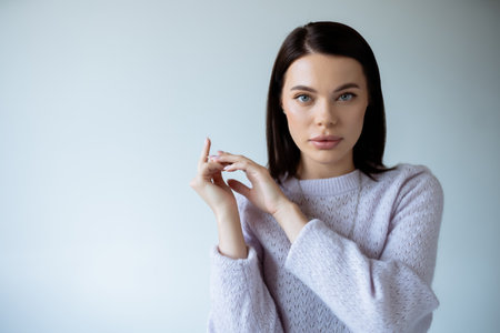 pretty young woman in soft knitted sweater looking at camera isolated on grey