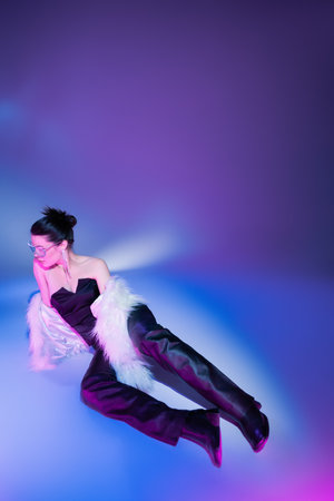 full length of brunette woman in black leather pants and white faux fur jacket lying on purple...
