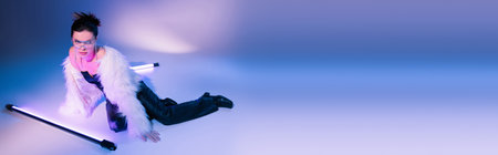 seductive woman in black leather pants and white furry jacket posing near lamps on blue and purple...