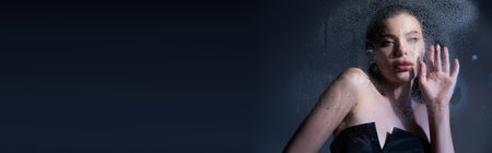 Young stylish woman in corset touching wet glass on grey background, bannerの写真素材