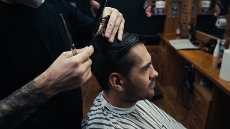 Tattooed hairdresser combing hair of client in barbershopの写真素材