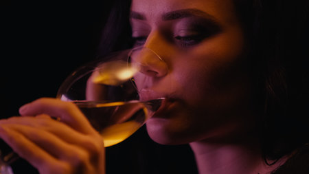Young woman drinking white wine from glass isolated on blackの写真素材