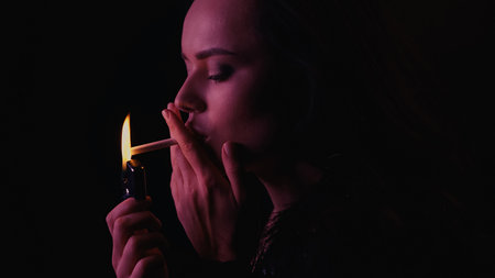Young woman holding lighter and cigarette isolated on black with lightingの写真素材