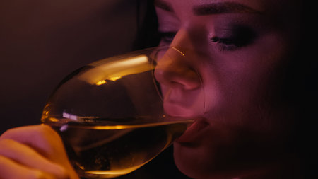 Young woman drinking wine on black background with lightingの写真素材