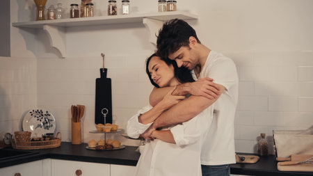 happy man with closed eyes embracing sensual girlfriend in kitchenの写真素材