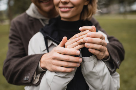 cropped view of caring young man in coat warming up hands of cheerful girlfriend in autumnal parkの写真素材