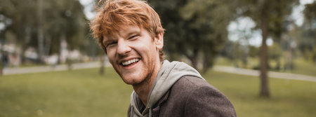 cheerful and redhead man in autumnal outfit smiling in park, bannerの写真素材