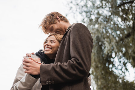 low angle view of redhead man kissing head of cheerful blonde woman during date in parkの写真素材