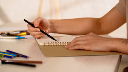 Partial view of tattooed woman holding pencil near sketchbook at home
