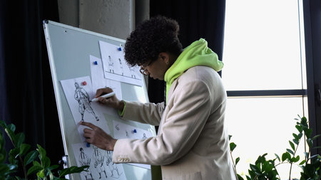 Side view of african american designer drawing sketches on flip chart in studio
