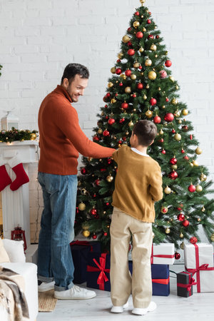cheerful father with son decorating green pine with christmas balls near gift boxesの写真素材