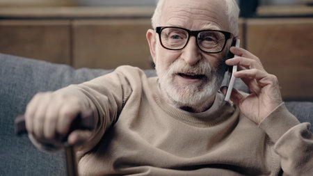 bearded senior man in eyeglasses talking on smartphone at homeの写真素材
