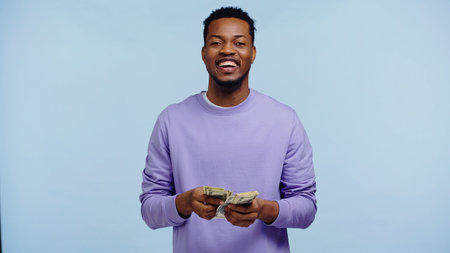 happy african american man counting dollar banknotes isolated on blue