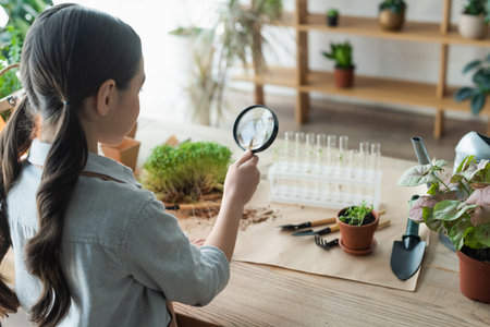 Girl holding magnifying glass near plants and test tubes at homeの写真素材