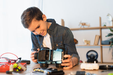 happy boy holding handmade car model near blurred parts on tableの写真素材
