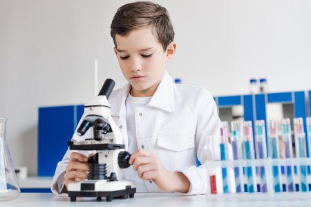 preteen boy in white coat near microscope and blurred test tubes in labの写真素材