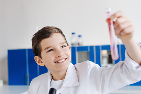 cheerful preteen boy looking at blurred test tube while making chemical experiment in labの写真素材