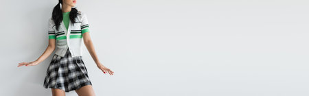 Cropped view of young woman in cardigan and plaid skirt standing on grey background, bannerの写真素材